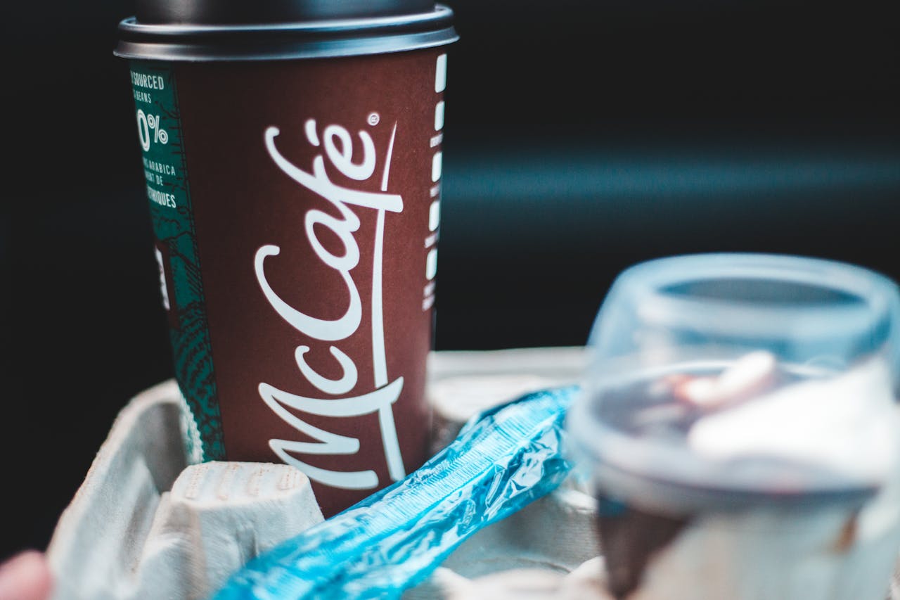 Delicious coffee in dark red cup with lid placed in cup holder with blue shiny wrapper and plastic cup